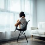 woman sitting on black chair in front of glass-panel window with white curtains