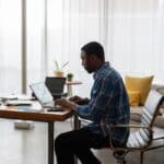 man in blue and white plaid dress shirt sitting on chair using laptop computer